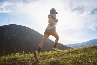 Dişi koşucu gün batımında dağlarda koşuyor. 