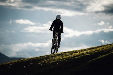Uçsuz bucaksız gökyüzünün altındaki engebeli dağlara bakan yeşil bir yamaçta bisiklet pedalları.