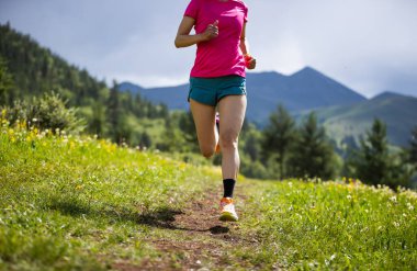 Dağlarda koşarken spor ayakkabılar ve spor giysiler giyen birinin kırpılmış görüntüsü.  