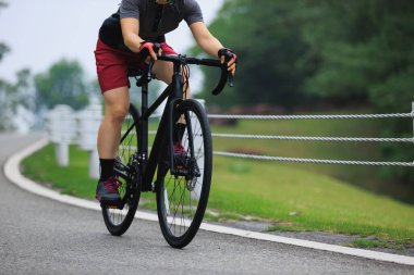 Kadın asfalt yolda bisiklet sürüyor. 