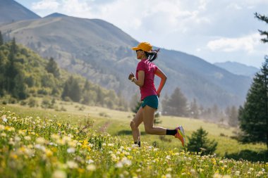 Dağların yeşil yamacında koşan aktif bir kadın. 