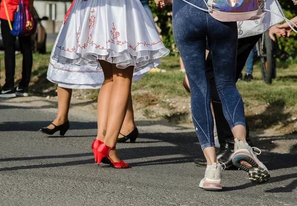 Beyaz ipekli, kırmızı, desenli etekli, kırmızı ayakkabılı, diğerleriyle dans edip el ele tutuşan bir kız.