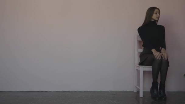 椅子に座り 白い灰色の背景の椅子の隣に立っている女の子 — ストック動画