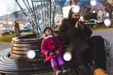 Sakallı adam kızla smartphone kullanarak bankta oturan