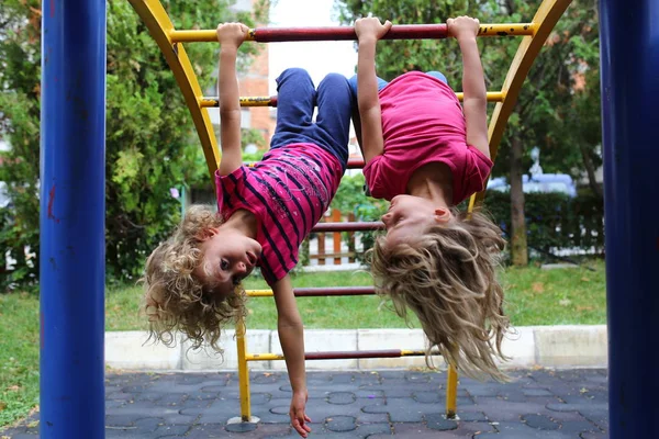 Two girls hanging on rails on playground