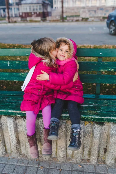 Ragazze Cappotti Rosa Baciare Seduti Sulla Panchina — Foto Stock