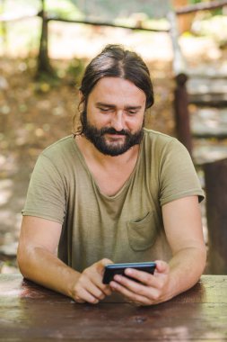 Park masadaki bankta oturmuş smartphone kullanan Genç sakallı adam görünümü Kapat