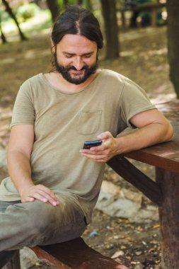 Sakallı adam parkta Smartphone kullanarak gülümseyen