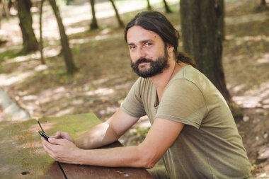 Park masadaki bankta oturmuş smartphone kullanan Genç sakallı adam görünümü Kapat