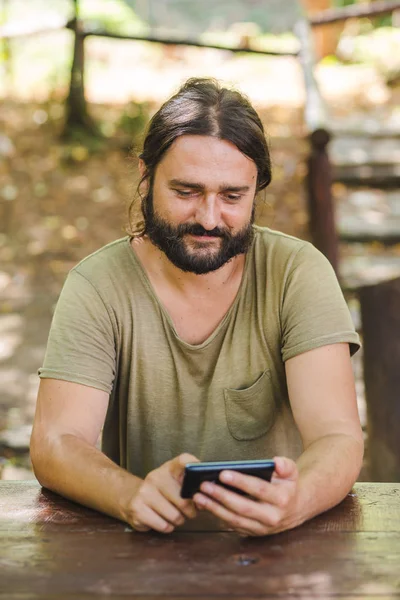 Park masadaki bankta oturmuş smartphone kullanan Genç sakallı adam görünümü Kapat