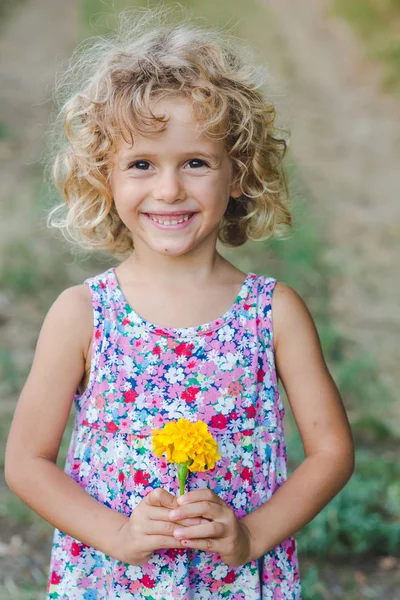 Portrait of smiling curly girl posing with yellow marigold flower