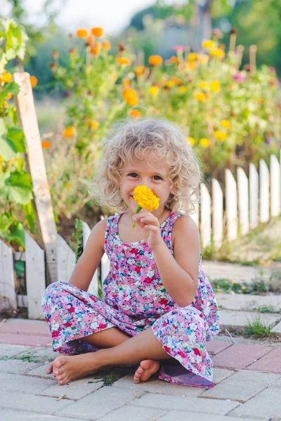 黄色のマリーゴールドの花の庭に座っている巻き毛の少女の笑顔 — ストック写真