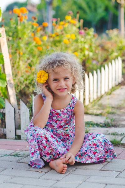 黄色のマリーゴールドの花の庭に座っている巻き毛の少女の笑顔 — ストック写真