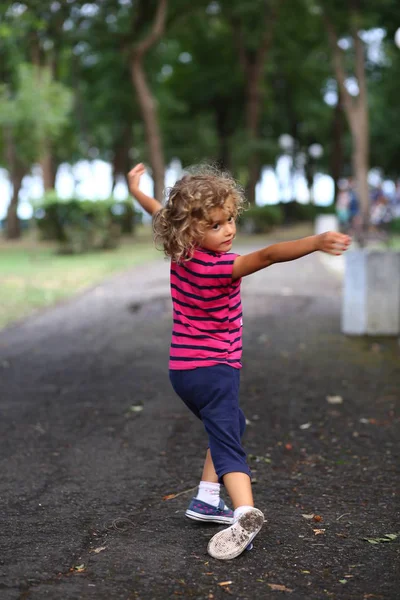 Portrait of curly girl in striped shirt dancing in city park.