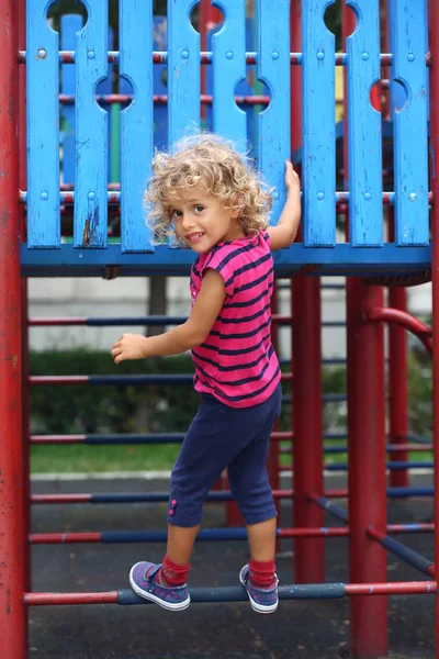 Çizgili tişört kadar oyun üzerinde metalik yapısı üzerinde tırmanma içinde sevimli kıvırcık kız.