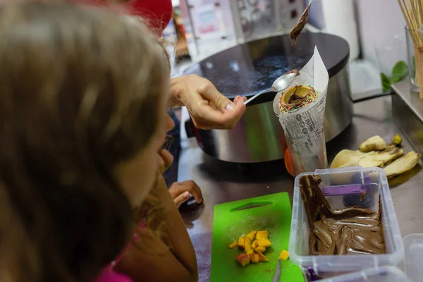 little girls making chimney cake in restaurant kitchen, with nonpareils and brown sugar