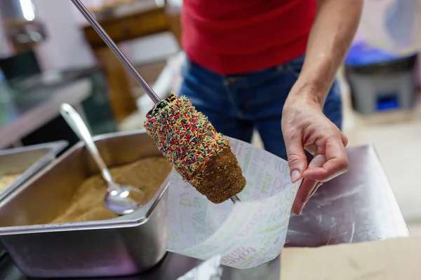 Woman making chimney cake in restaurant kitchen, with nonpareils and brown sugar. Closeup photo, no face.