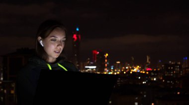 Genç kadın gece şehrinde dizüstü bilgisayara bakıyor.