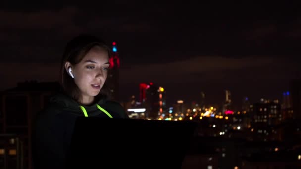 Genç kadın gece şehrinde dizüstü bilgisayara bakıyor. — Stok video