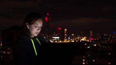 Genç kadın gece şehrinde dizüstü bilgisayara bakıyor.