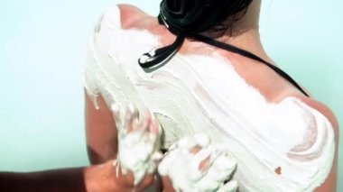 Tanımlanamayan kişi, kadının arkasına beyaz kil sürüyor.