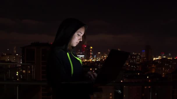 Genç kadın gece şehrinde dizüstü bilgisayara bakıyor. — Stok video