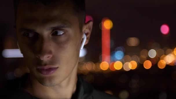 Junger Mann mit Kopfhörern schaut sich nachts um — Stockvideo