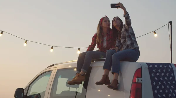 Genç kadınlar arabanın üstünde selfie çekiyorlar.