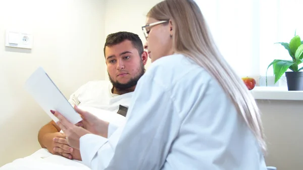 Doctor with tablet communicating with patient in hospital ward