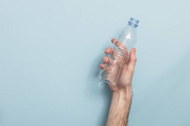 Mavi bir arka plan karşı geri dönüşüm boş plastik şişe tutan el