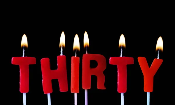 Thirty spellt out in red birthday candles against a black background — Stock Photo, Image