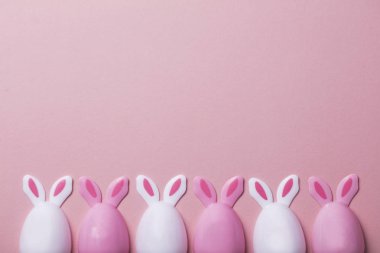 Paskalya yumurtaları pastel pembe bir arka plan üzerinde tavşan kulaklı
