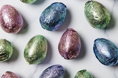Paskalya yumurtası çikolata mermer arka planda parlak renkli folyo sarılmış davranır
