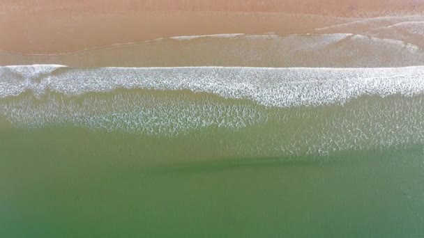 Vista sobre una hermosa costa mientras las claras olas azules irrumpen en una playa de arena — Vídeo de stock