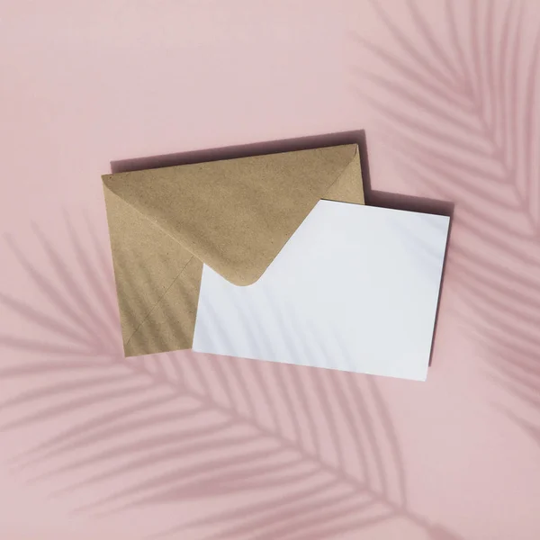Ombre de feuille de palmier d'été sur carte blanche vierge et enveloppe en papier brun maquette — Photo