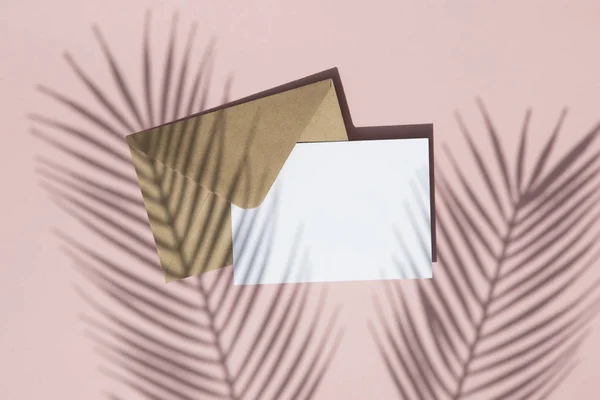 Літня тінь пальмового листя на порожній білій картці і коричневий паперовий конверт глузують — стокове фото
