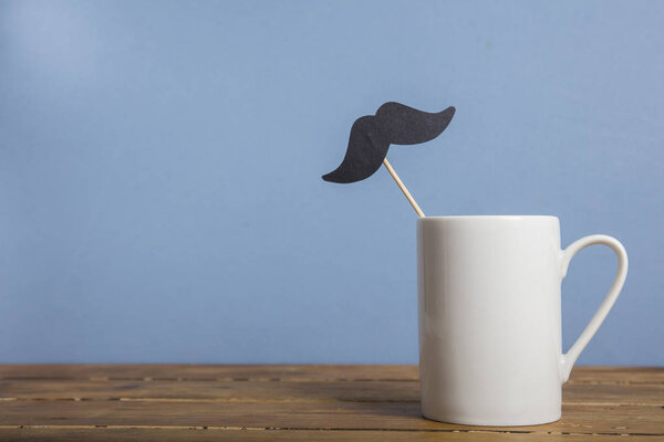 Кофейная кружка с бумажными усами на синем фоне
