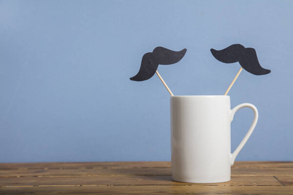 Кофейная кружка с бумажными усами на синем фоне
