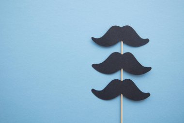 Mavi arka plan üzerinde siyah kağıt bıyık. Babalar günü veya mens sağlık kavramı