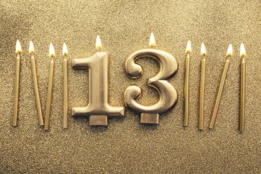 Number 13 gold celebration candle on a glitter background clipart
