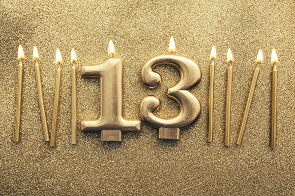 Number 13 gold celebration candle on a glitter background — Stock Photo, Image