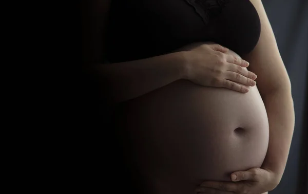 Mulher grávida segurando uma colisão do bebê contra um fundo escuro — Fotografia de Stock