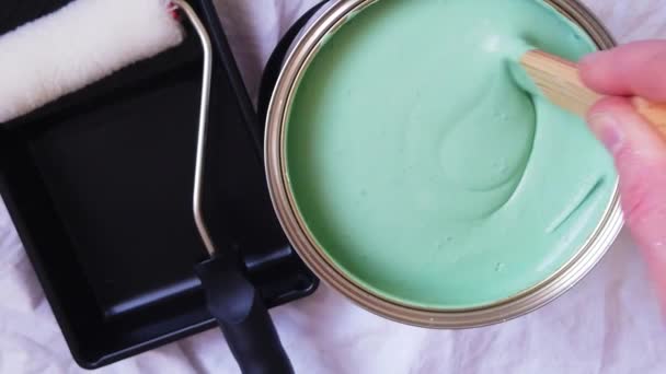 Une personne mélangeant un pot de douleur verte à côté d'un rouleau de peinture et d'un plateau. Mouvement lent — Video