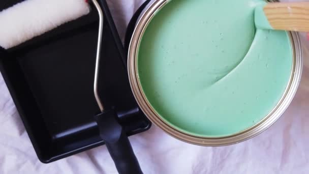 Una persona que mezcla una olla de dolor verde al lado de un rodillo de pintura y bandeja. Movimiento lento — Vídeos de Stock