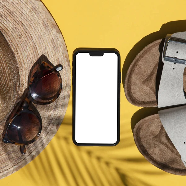 Summertime composition. Blank smartphone with summer accessories and palm shadow