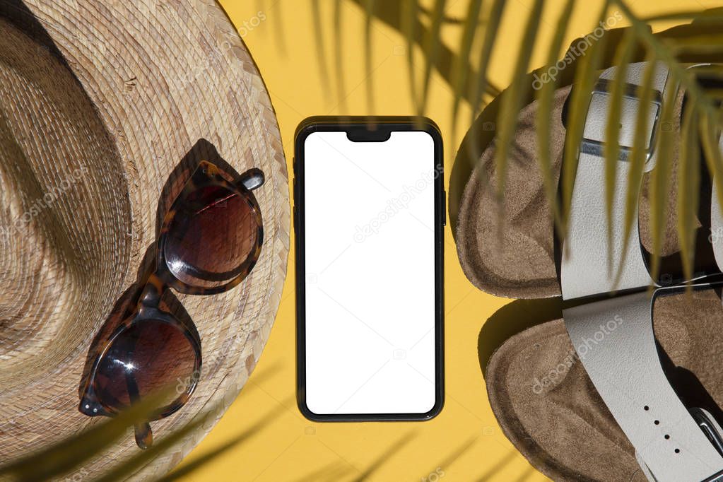 Summertime composition. Blank smartphone with summer accessories and palm shadow