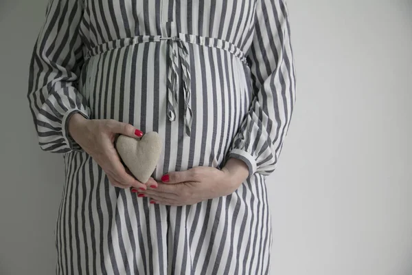 Kobieta w ciąży trzyma kształt serca przed tutaj baby bump — Zdjęcie stockowe
