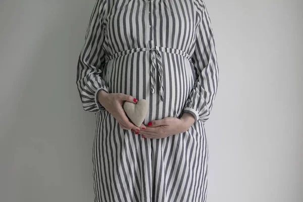 En gravid kvinna som innehar en hjärtform framför här baby bump — Stockfoto