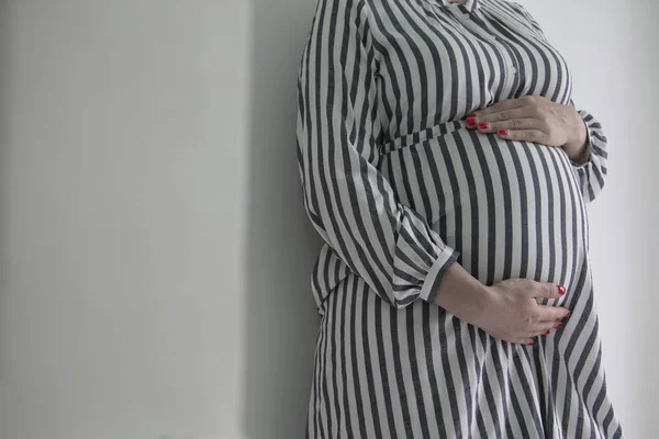 Bebeğini yumru tutan hamile bir kadın düz bir arka plan aleyhine durdu — Stok fotoğraf