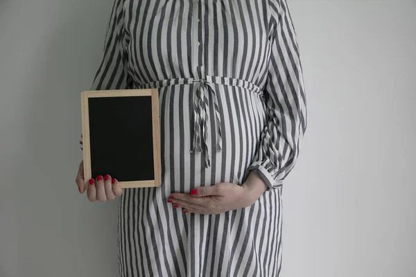 Uma mulher grávida segurando um quadro preto perto de sua barriga grávida — Fotografia de Stock